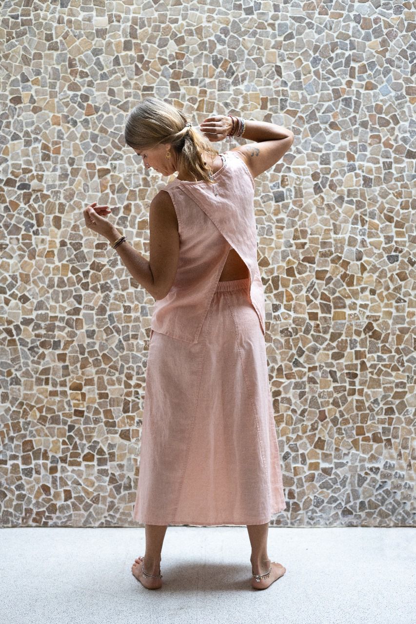 A woman wearing a sleeveless pink back split top and a matching skirt made by Shivani Divine Wear and standing against a textured wall. Back view.