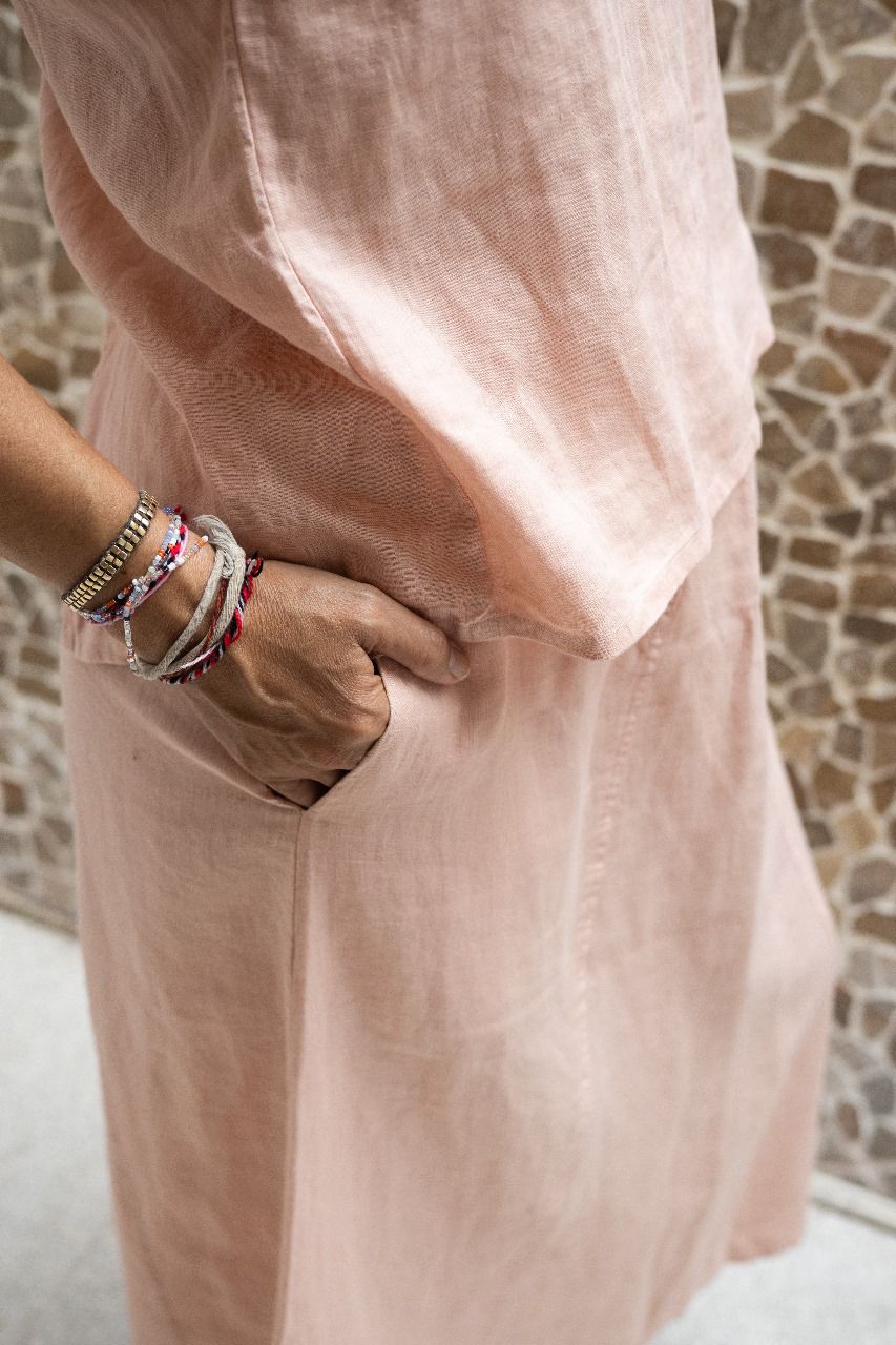 A woman wearing a sleeveless pink top and a matching skirt standing against a textured wall. Detail.