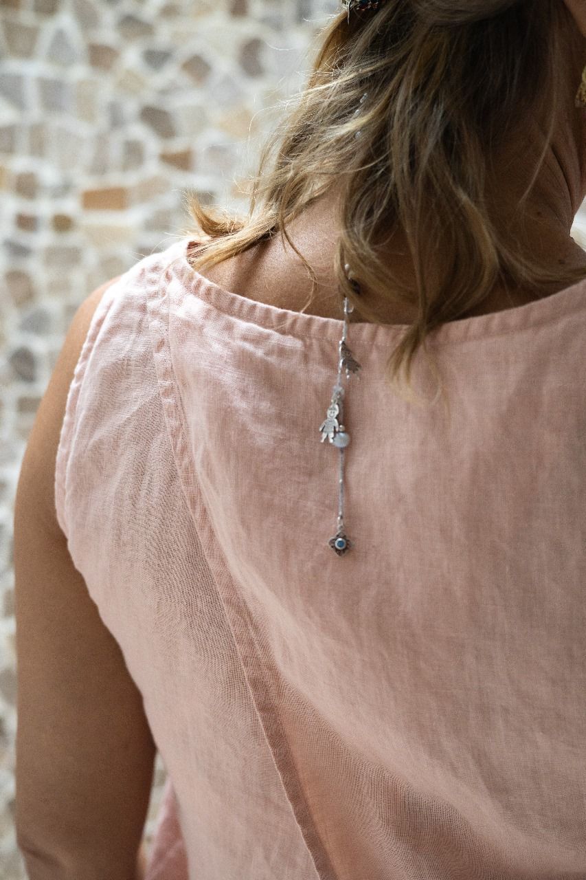 A woman wearing a sleeveless pink top standing against a textured wall. Detail.