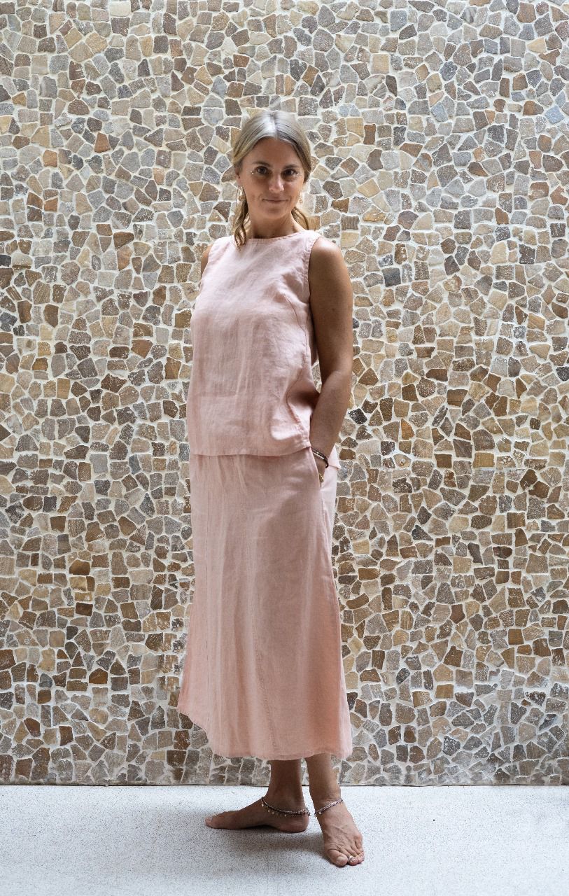 A woman wearing a sleeveless pink top and a matching skirt made by Shivani Divine Wear and standing against a textured wall.