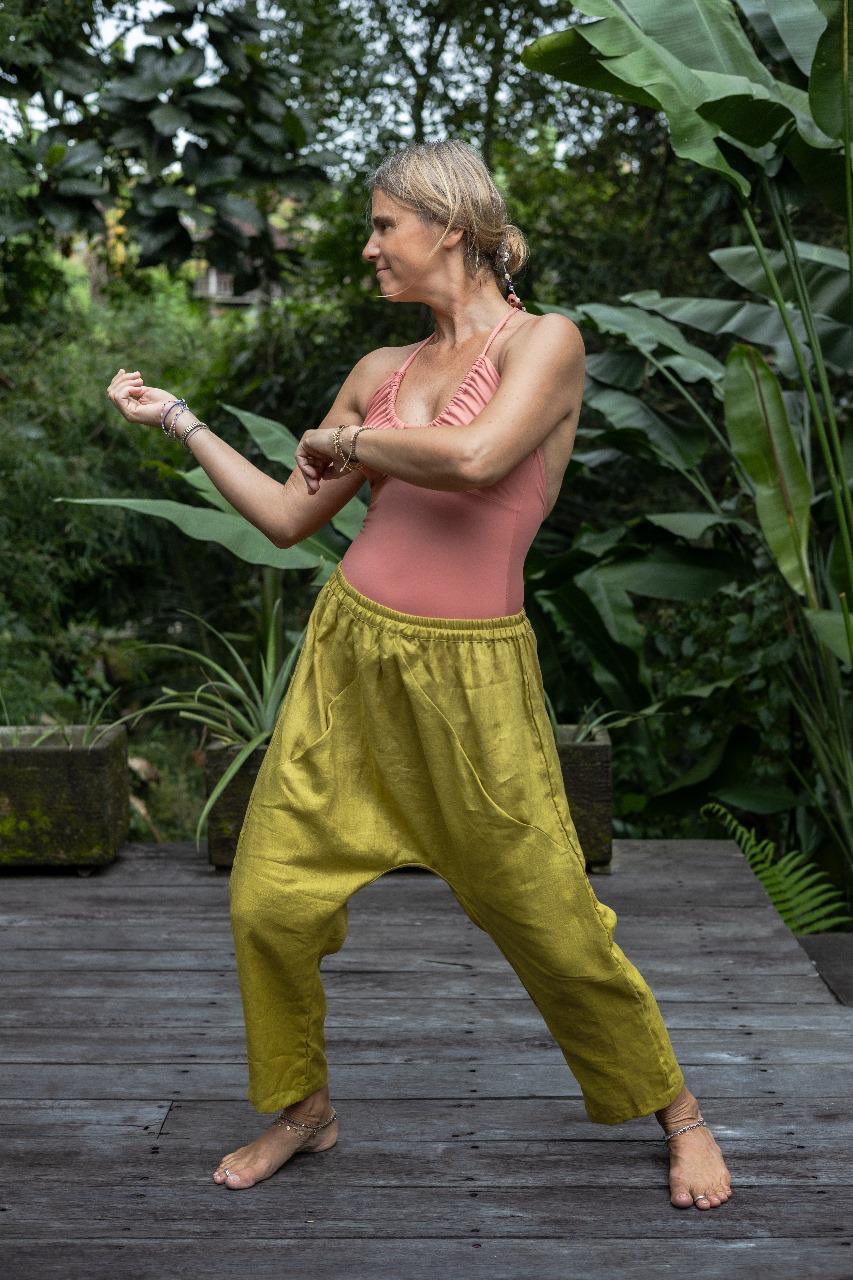A woman standing against a lush green backdrop, wearing lemon green linen hipster pants and a monokini. All Shivani Divine Wear.