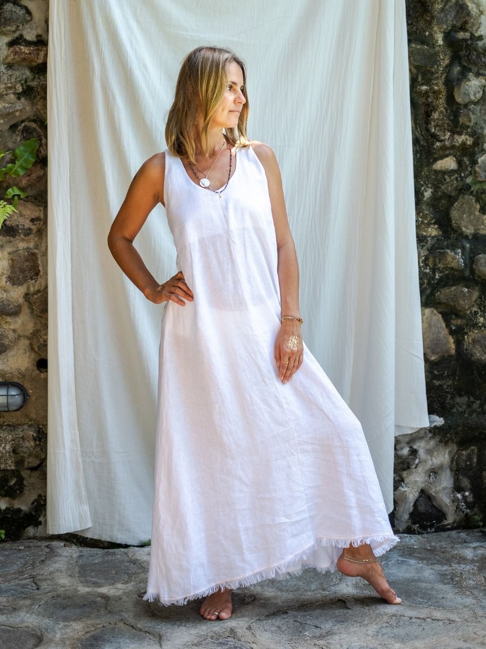 A woman wearing a white maxi v-neck linen dress, posing in front of a white backdrop.