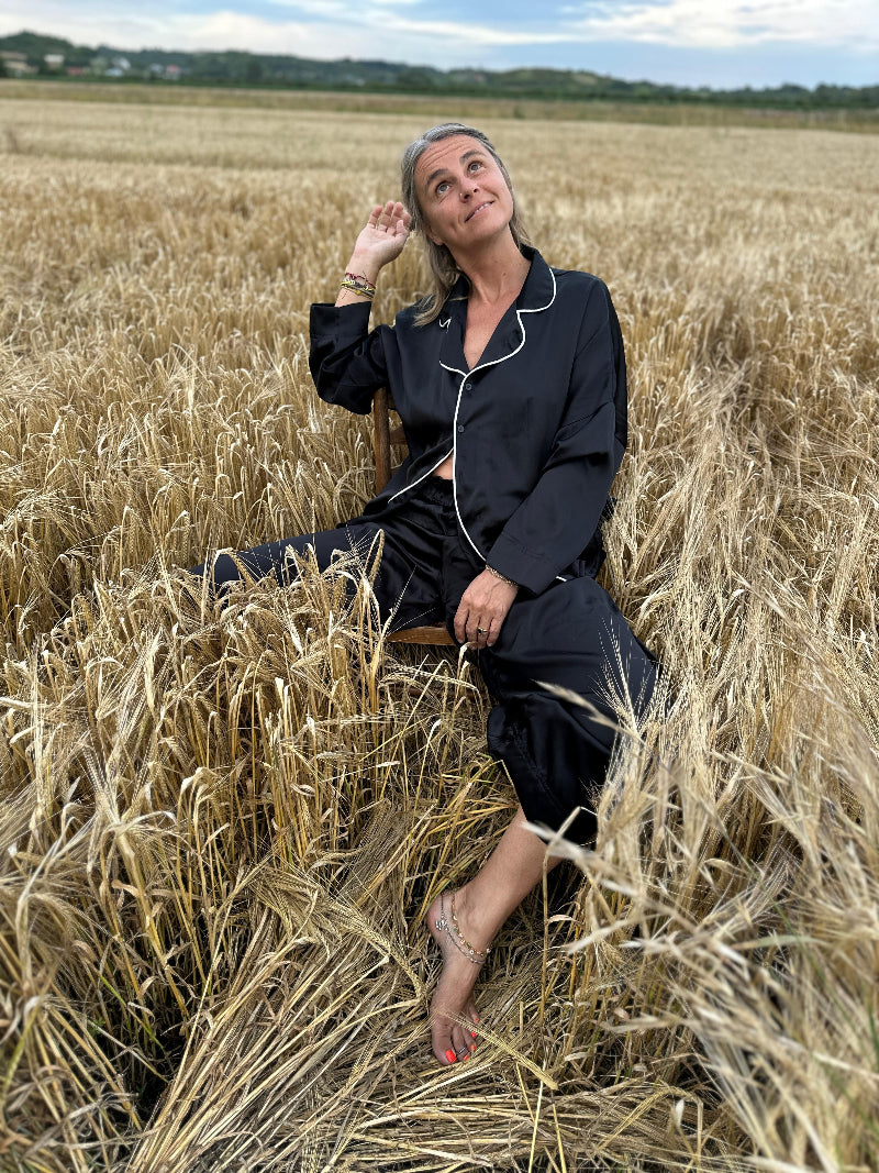 A queen in black silk sits in the heart of the harvest, her gaze soft yet unshakable, framed by the endless horizon and a sky ready to rain blessings.