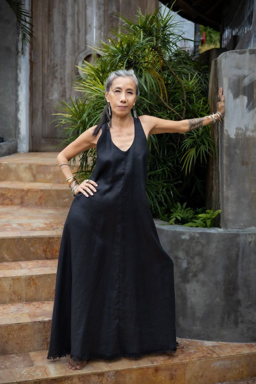 A woman standing on outdoor steps, in a black flowing linen dress, with one arm extended to the wall