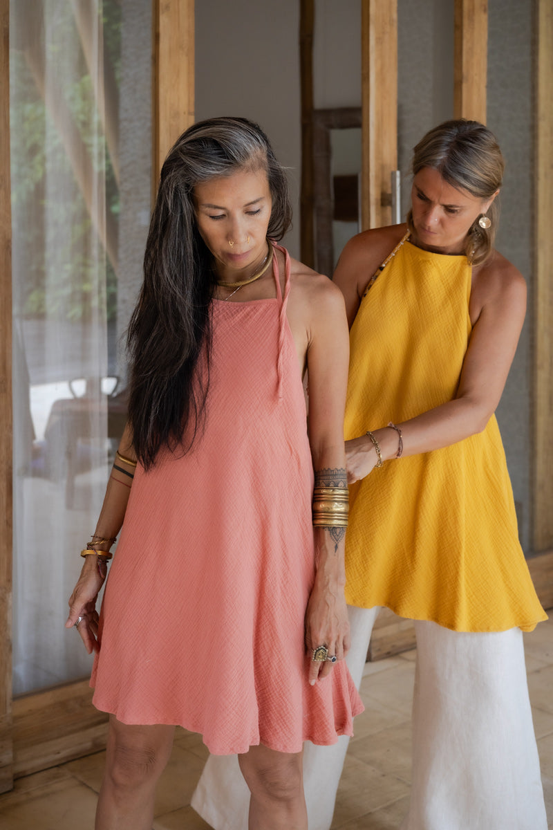 2 women wearing open back tie cotton dresses with a texture in yellow and rose colors- standing next to each other.