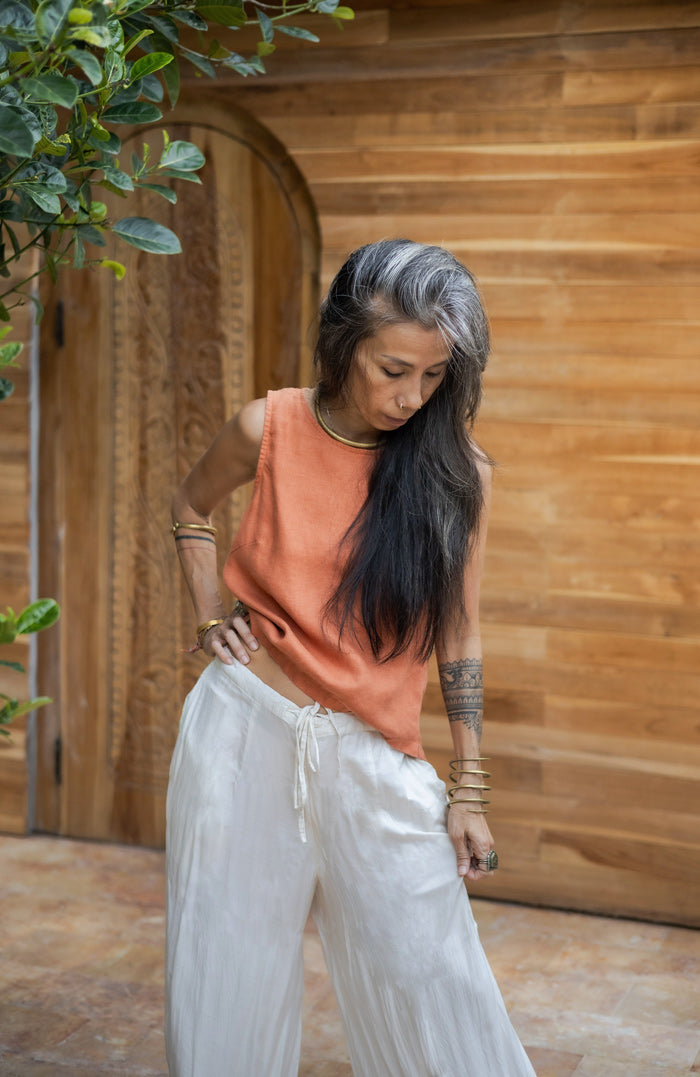 A woman with long hair modeling silk white pants and a rose colored linen sleeveless top .