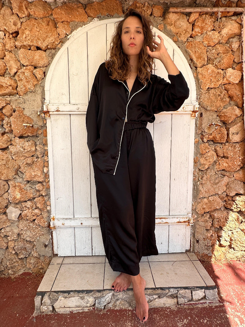 Woman in a black shivani pajama set outfit standing in front of a white archway on a stone wall.