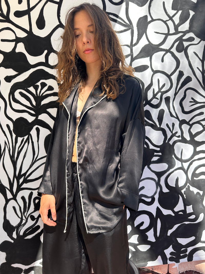 Person wearing Shivani black silk pajama outfit against a black and white abstract patterned wall.