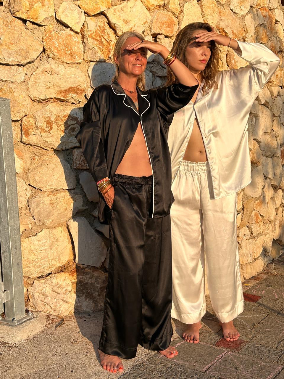 Two people in black and white shivani pajamas standing against a stone wall.