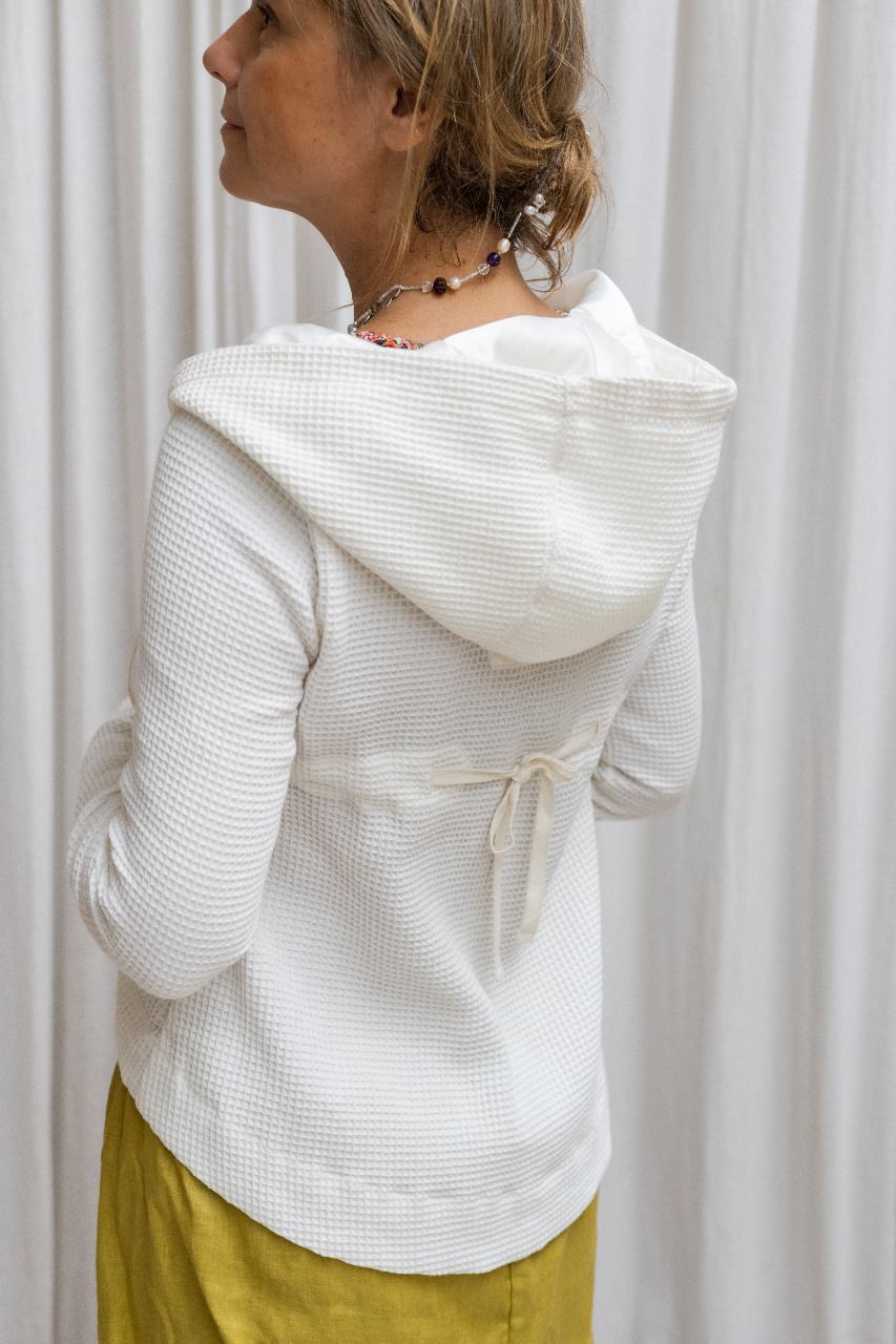 A woman wearing a white hoodie with a zipper and a flowing hood, paired with yellow pants. Back view