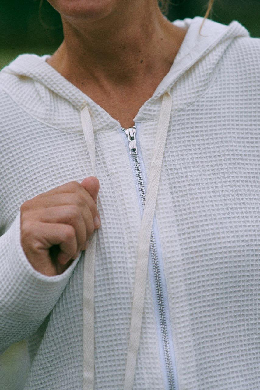 A woman wearing a white hoodie with a zipper, detail view.
