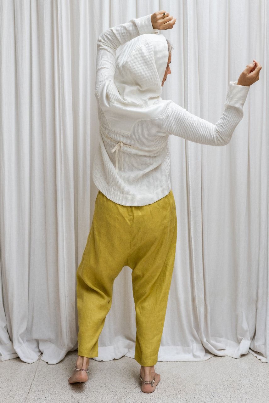 A woman wearing a white hoodie with a zipper and a flowing hood, paired with yellow pants. Back view.