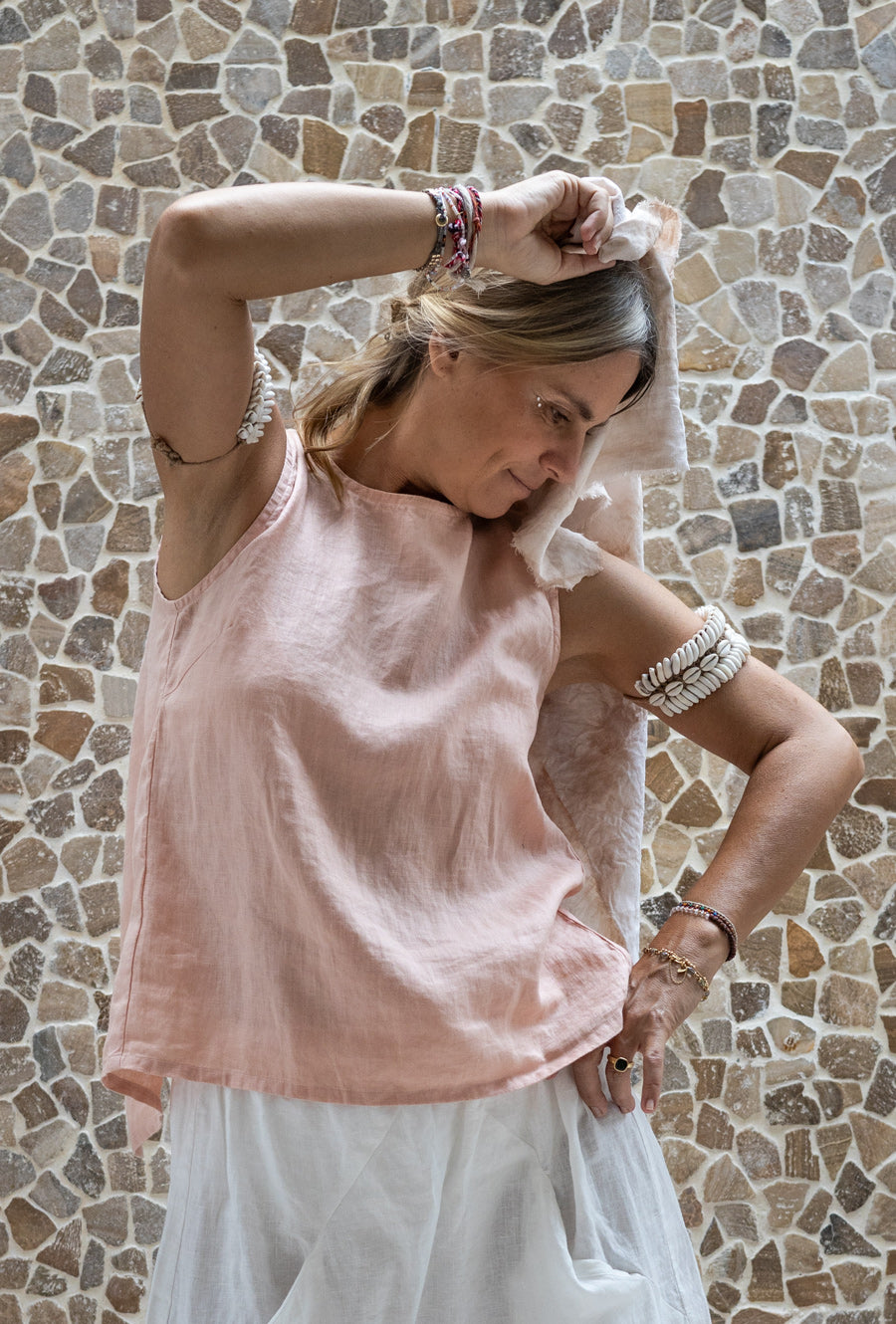 A person wearing a sleeveless crew-neck top in a warm rose color, standing against a textured wall.