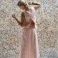 A woman wearing a sleeveless pink back split top and a matching skirt made by Shivani Divine Wear and standing against a textured wall. Back view.
