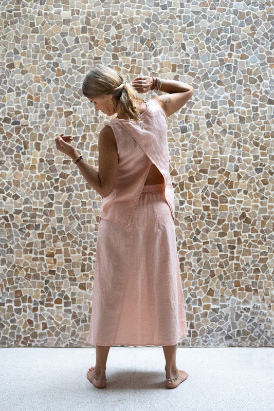 A woman wearing a sleeveless pink back split top and a matching skirt made by Shivani Divine Wear and standing against a textured wall. Back view.