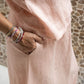 A person wearing a rose colored midi skirt with a flowing A silhouette, standing in front of a textured wall in the background. - Detail