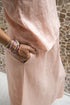 A woman wearing a sleeveless pink top and a matching skirt standing against a textured wall. Detail.