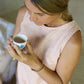 A person wearing a sleeveless crew-neck top in a warm rose color, sitting on the floor, holding a cup of tea, photographed from above.