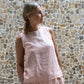 A person wearing a sleeveless crew-neck top in a warm rose color, with an open-back design from Shivani Divine Wear, standing against a textured wall.