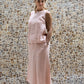 A woman wearing a sleeveless pink top and a matching skirt made by Shivani Divine Wear and standing against a textured wall.