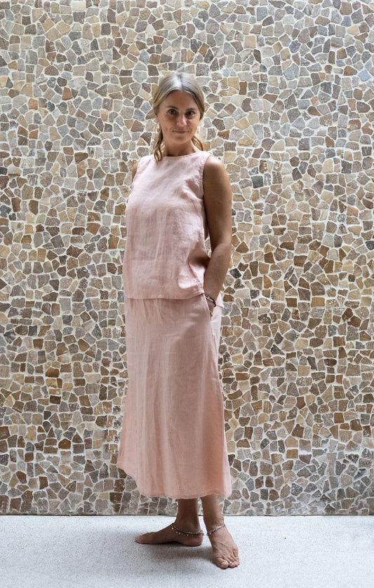A woman wearing a sleeveless pink top and a matching skirt made by Shivani Divine Wear and standing against a textured wall.