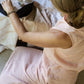 A woman wearing a sleeveless rose pink top and a matching skirt sitting on the floor, serving tea, photographed from above. 