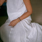 A woman wearing a sleeveless white top and a matching skirt sitting on the floor, front view. 