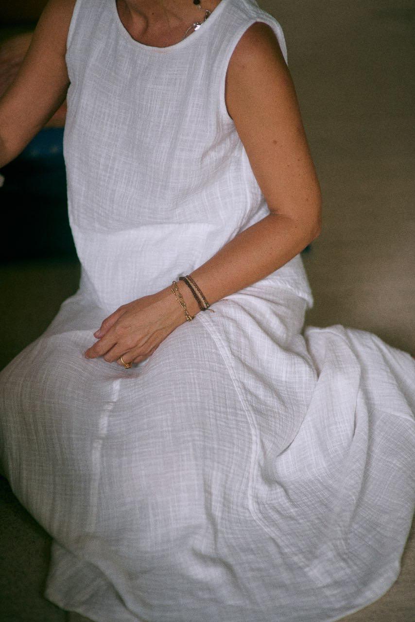A woman wearing a sleeveless white top and a matching skirt sitting on the floor, front view. 