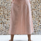 A person wearing a rose colored midi skirt with a flowing A silhouette, standing in front of a textured wall in the background.