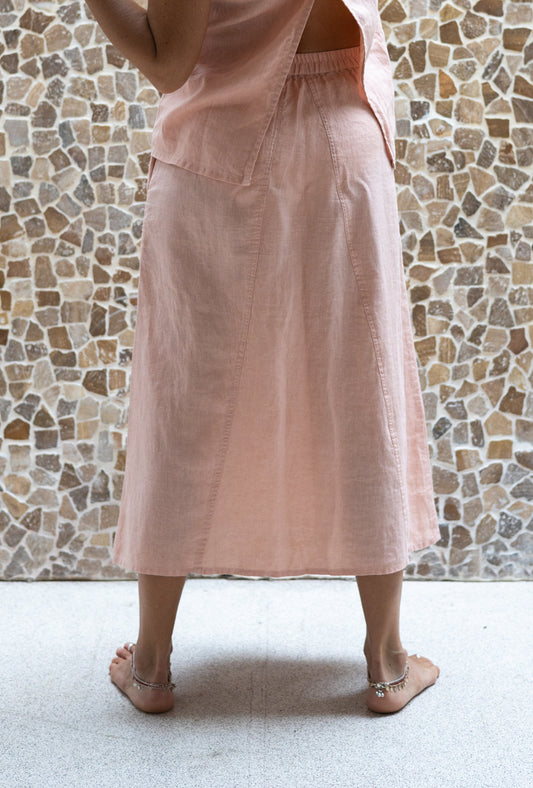 A person wearing a rose colored midi skirt with a flowing A silhouette, standing in front of a textured wall in the background.