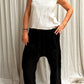 A woman standing against a white backdrop, wearing black linen hipster pants and sleeveless cotton top. Front view.