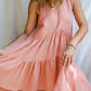 A woman in a rose color asymmetric cotton dress with a sleeveless design standing in front of a white fabric backdrop.