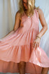 A woman in a rose color asymmetric cotton dress with a sleeveless design standing in front of a white fabric backdrop.