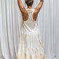 A person wearing a sleeveless, asymmetric hemline silk dress in front of a white background. Back view.