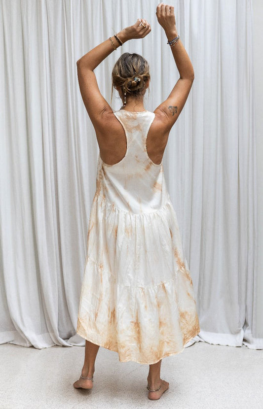 A person wearing a sleeveless, asymmetric hemline silk dress in front of a white background. Back view.