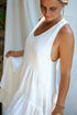 A woman in a white asymmetric cotton dress with a sleeveless design standing in front of a white backdrop, close up.