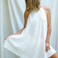 A woman wearing a white, open back tie cotton dress with a texture that drapes over the body.