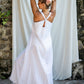 A woman wearing a white maxi v-neck linen dress, posing in front of a white backdrop, back view.
