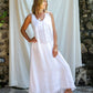 A woman wearing a white maxi v-neck linen dress, posing in front of a white backdrop.