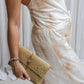 A woman wearing a beige tea-dye elegant silk romper with a halter-style neckline and wide-leg silhouette, standing with a white backdrop in the background. Close up view.