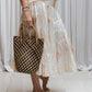 A woman wearing a tea dye silk skirt with a gathered tiered design and an elasticized waistband, paired with a white sleeveless top. Holding a small bag 