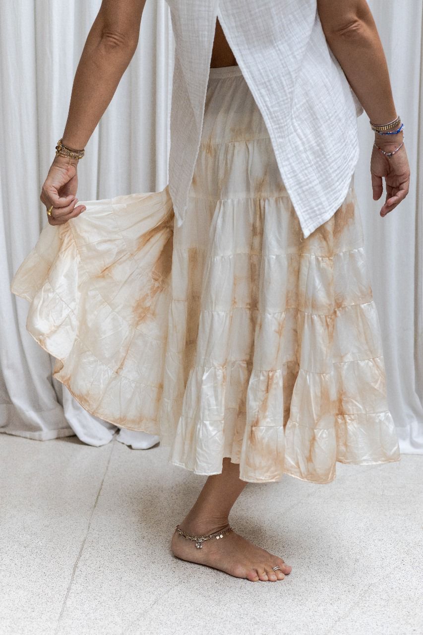 A woman wearing a tea dye silk skirt with a gathered tiered design and an elasticized waistband, paired with a white sleeveless top. Side view.