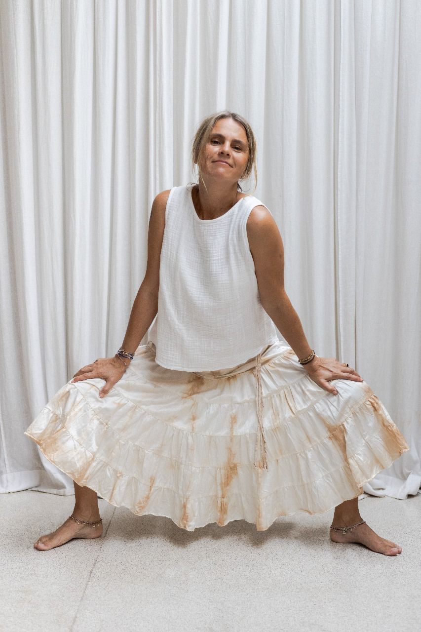 A woman wearing a tea dye silk skirt with a gathered tiered design and an elasticized waistband, paired with a white sleeveless top. Front view.
