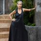 A woman standing on outdoor steps, in a black flowing linen dress, with one arm extended to the wall