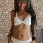 A woman wearing a white bra and mid-rise briefs, standing against a textured background.