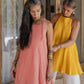 2 women wearing open back tie cotton dresses with a texture in yellow and rose colors- standing next to each other.