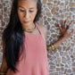 A woman wearing a rose color, open back tie cotton dress with a texture that drapes over the body.