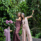 2 women wearing a rose pink and brown linen romper with wide legs and a V-neckline, standing in front of a lush green background.