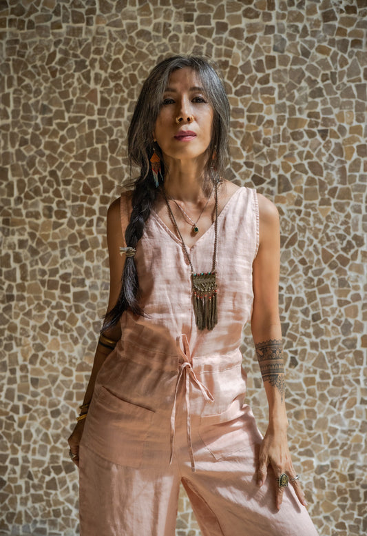 A woman wearing a rose pink linen romper with wide legs and a V-neckline, standing against a textured background.