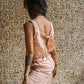 A woman wearing a rose pink linen romper with wide legs and a V-neckline, standing against a textured background. side view.